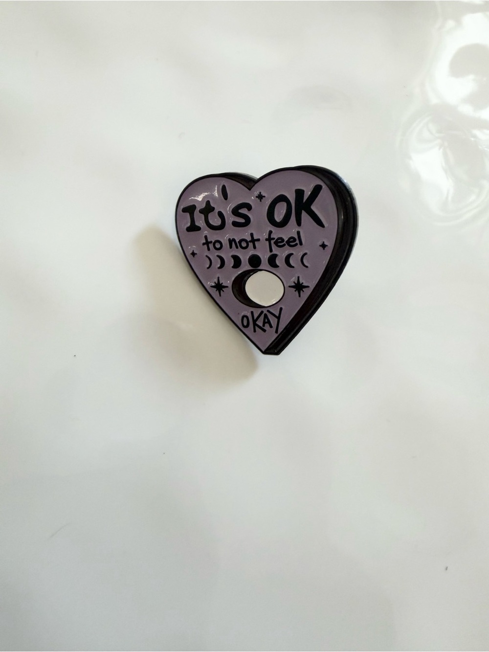 Purple heart pin with the words 'It's OK to not feel OKAY' and moon phases #ment